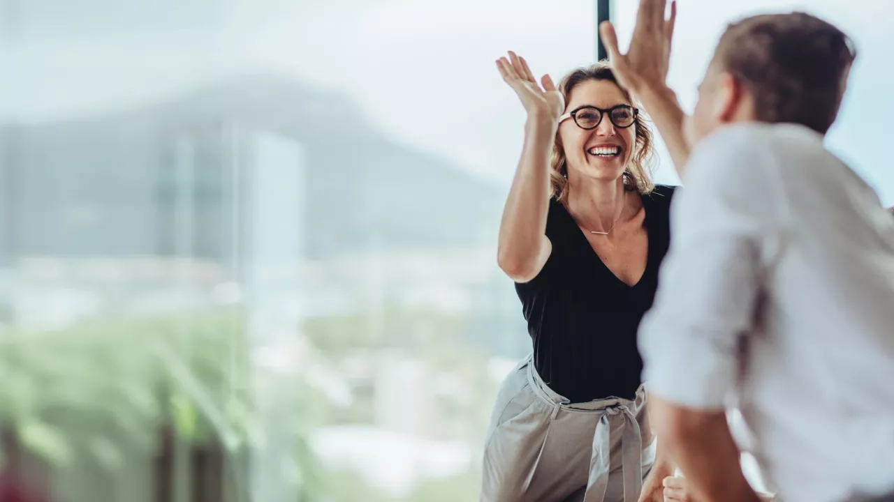 Businesswoman giving a high five to male colleague in meeting. Business professionals high five during a meeting in boardroom.