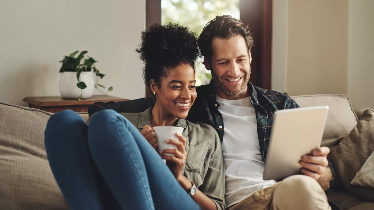 Husband and wife together on couch at home reviewing documents on a tablet screen