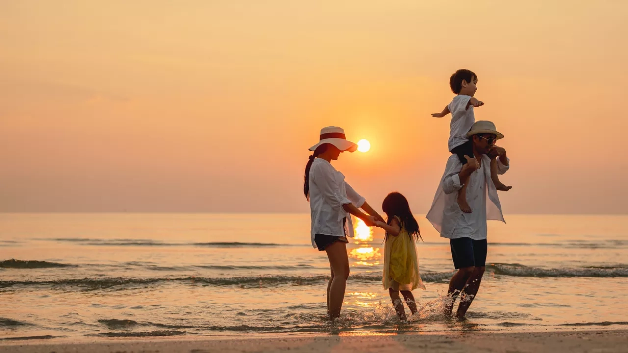 A happy family of four playing on the beach during sunset. 