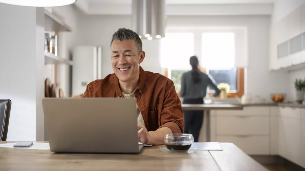 man smiling while working on his laptop in kitchen