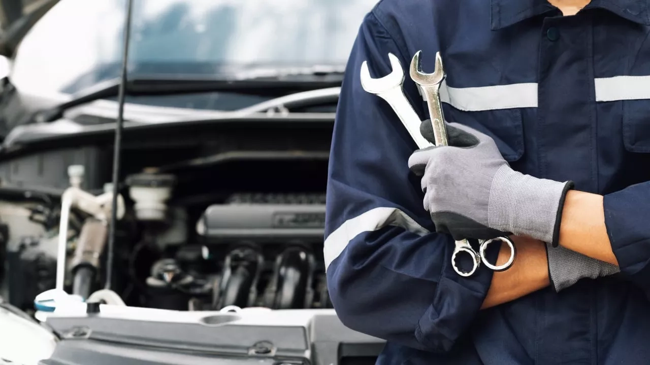 mechanic holding a wrench in front of a car