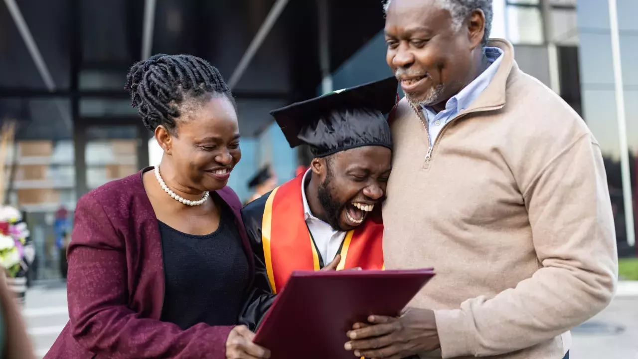 Mother and father hugging their graduating son holding a diploma in celebration