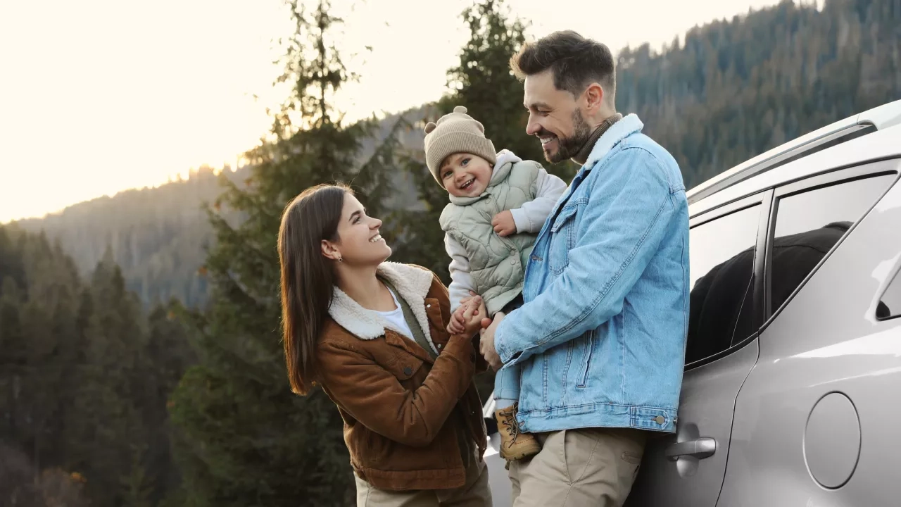 Parents and their daughter near car in mountains.