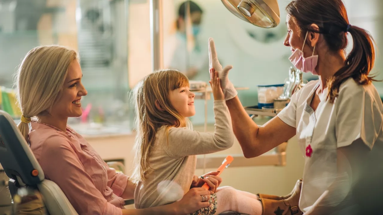 Mother and happy young girl hi-fiving dentist at dental checkup