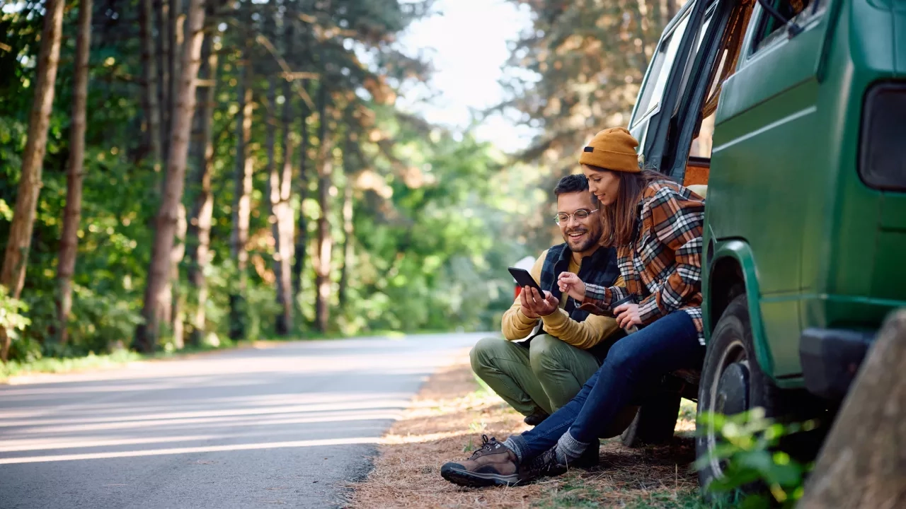 Two-campers-using-mobile-phone-while-traveling-with-their-van-in-nature