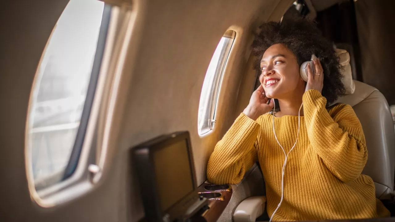 Young woman sitting on an airplane looking through the window listening to music