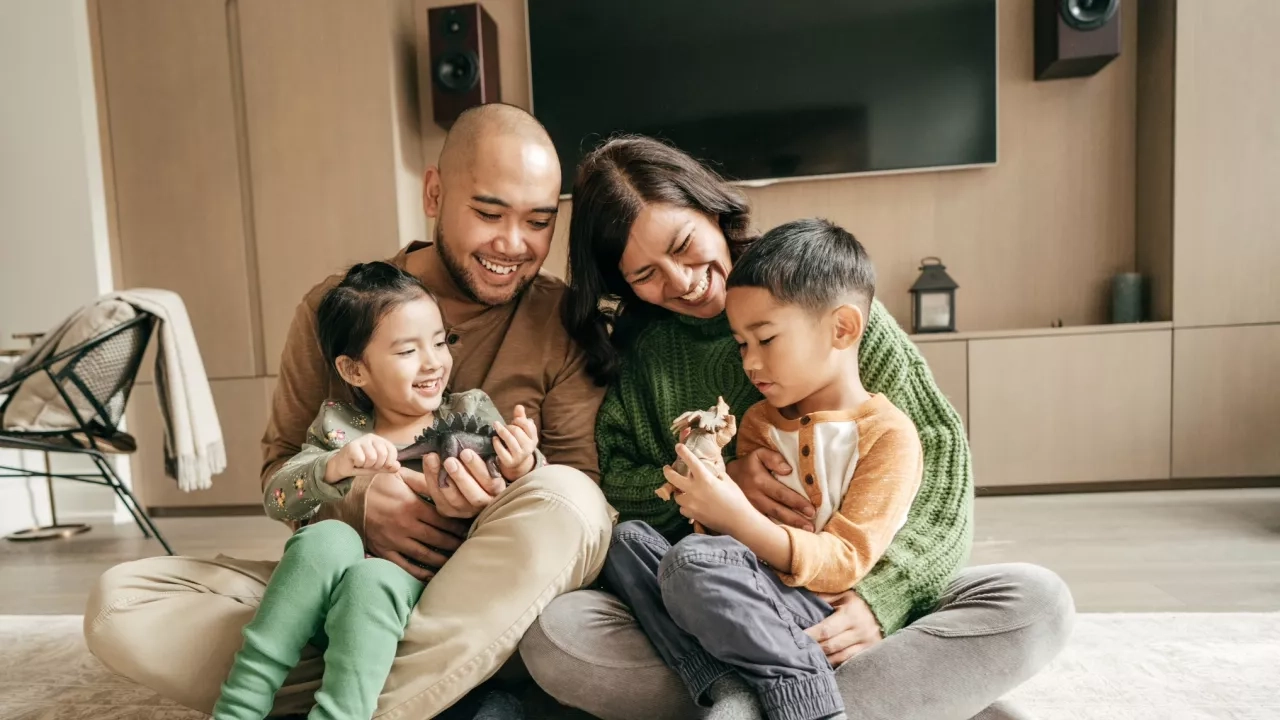 Family with young kids sitting in living room playing with dinosaur toys