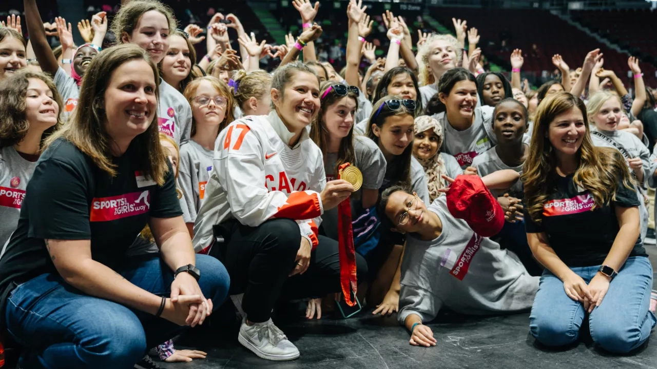 Olympic medalist showing off her medal surrounded by girls celebrating Sports Day the Girls Way
