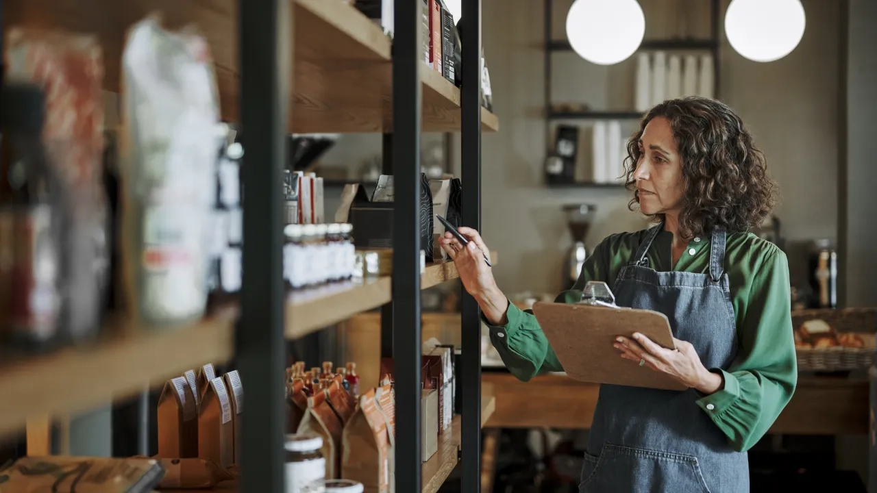 Mature deli owner taking inventory on store shelves using a clipboard 
