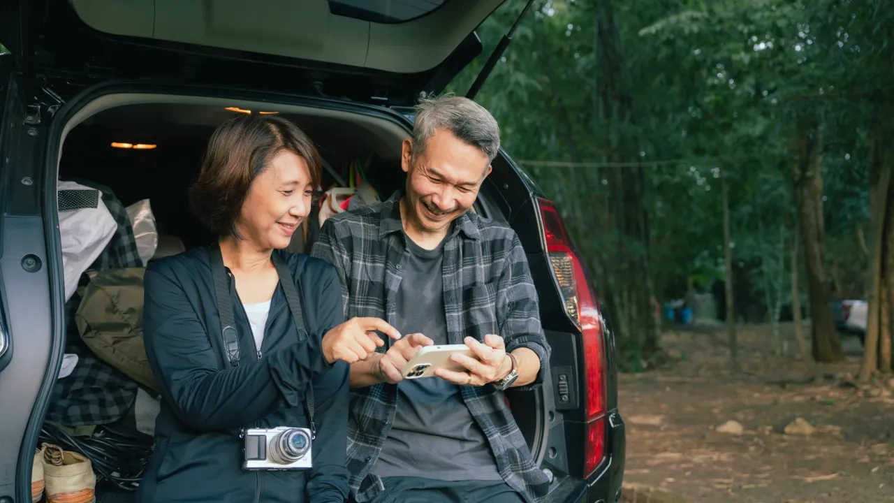 A couple using their phone by their packed car trunk in the forest