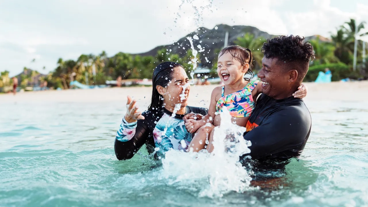 Young girl and adult friends splash in the ocean