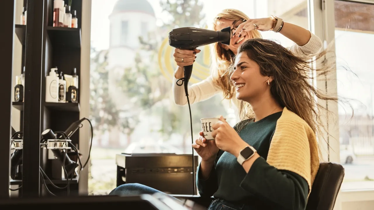 Young Woman Relaxing with Coffee While Getting Hair Styled in Salon