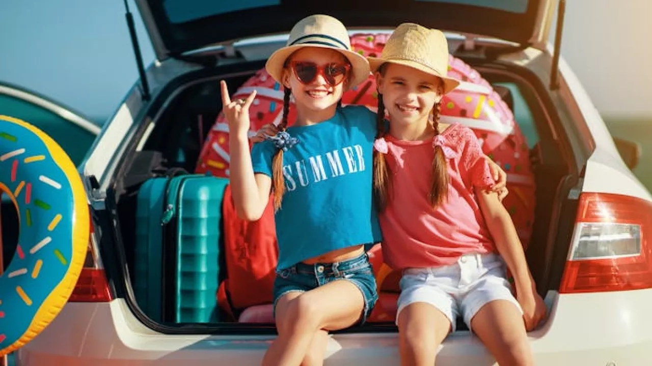 Two kids stting in open trunk of station wagon ready to go on a summer road trip