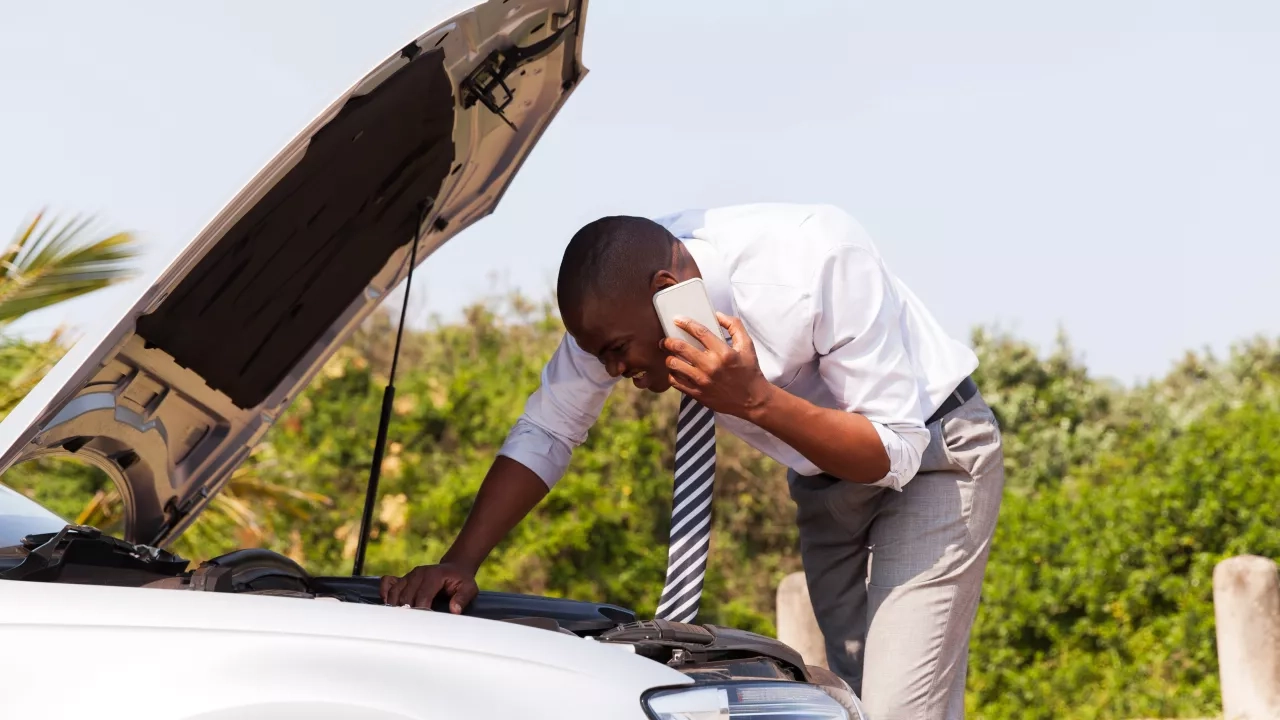 Business man on cell phone looking in hood of car