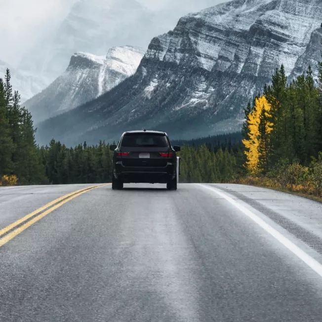 Car driving along the road with trees and mountains in the distance Car driving along the road with trees and mountains in the distance