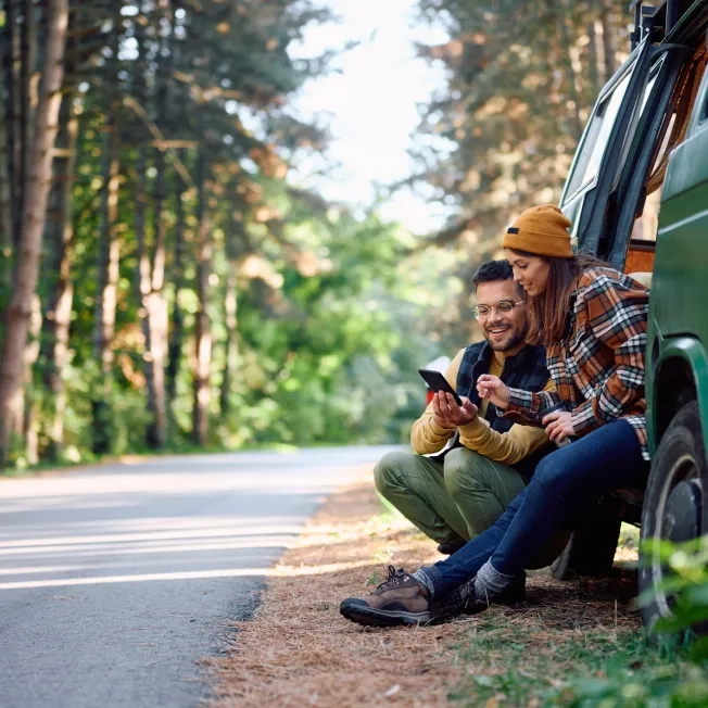 Two-campers-using-mobile-phone-while-traveling-with-their-van-in-nature