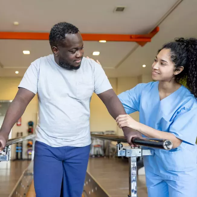 Man at physical therapy trying to walk along bars with assistance