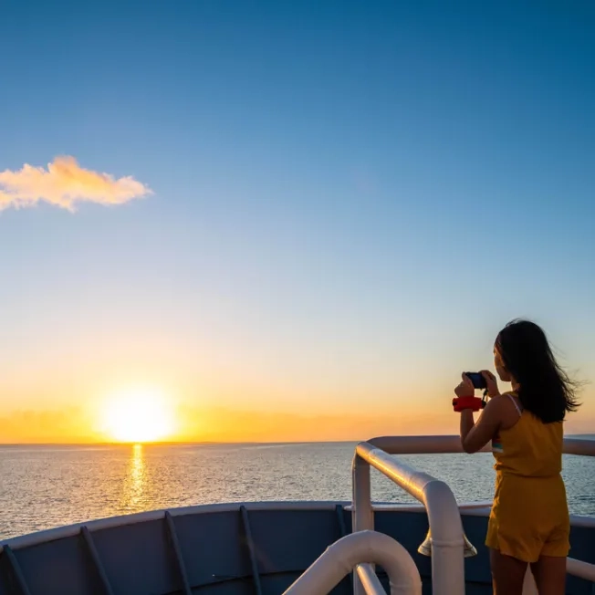 A child taking a photo off the National Geographic LIndblad Expeditions ship at sunset