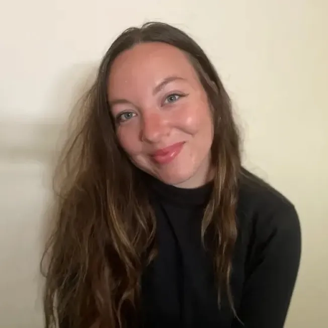 A girl faces the camera smiling in front of a plain background