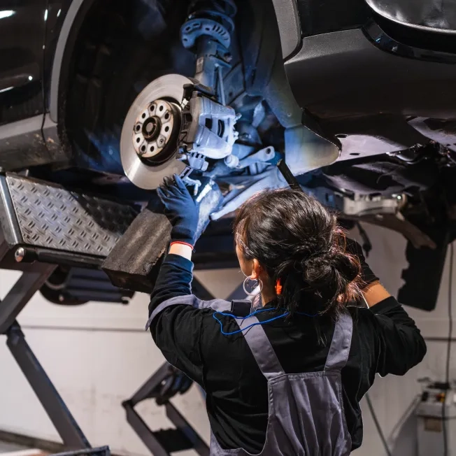 Female mechanic inspecting car brakes on hydraulic lift in repair shop