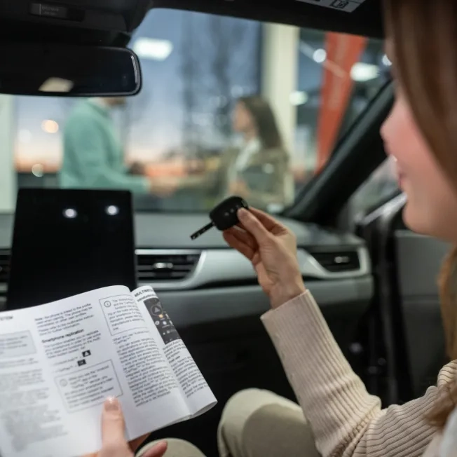 Woman holding car key and manual inside new vehicle