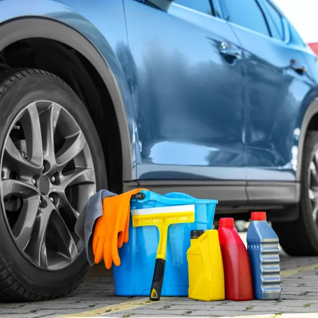 Car cleaning products and bucket near automobile outdoors on sunny day
