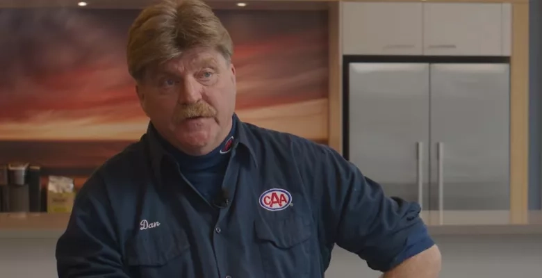 A man sits facing the camera wearing a CAA tow truck driver shirt