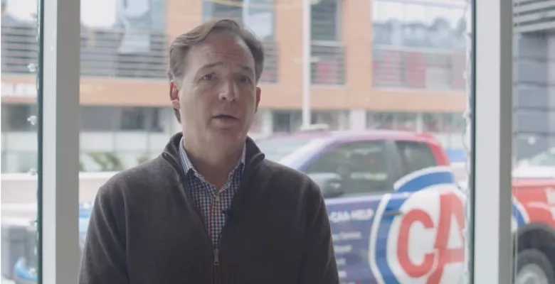 a man stands infornt of a windo with a CAA branded truck behind him 
