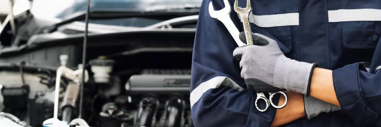 mechanic holding a wrench in front of a car