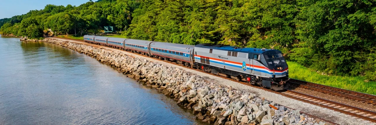 Amtrak Vacations train riding along the water and tree line