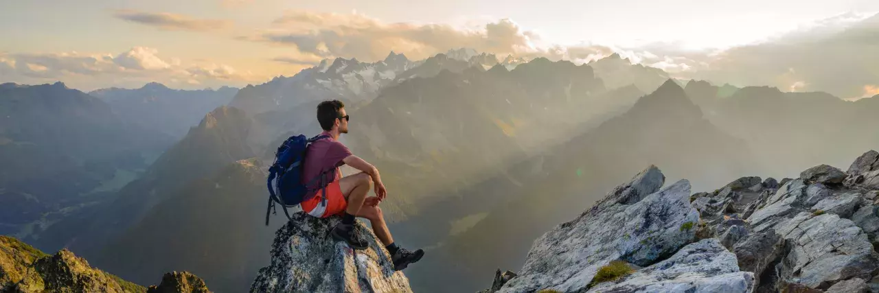 A man sitting on a rock at the summit of a mountain, admiring the scenery after a long hike in Switzerland.