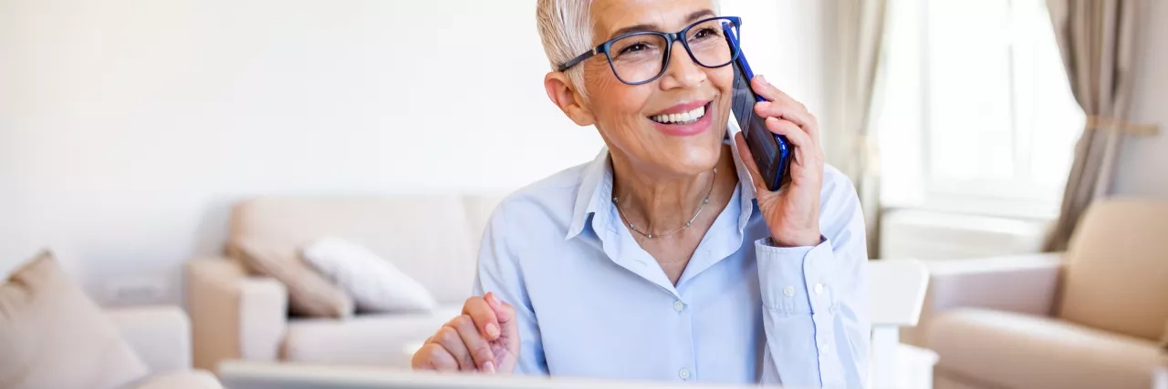 older woman talking on phone in front of laptop