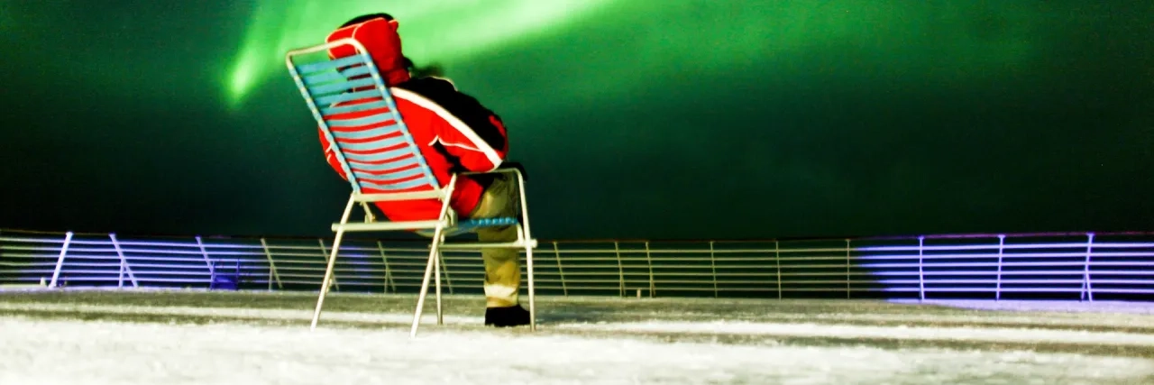 A person sitting on a chair on the deck of a Hurtigruten ship watching the Northern Lights in Norway.