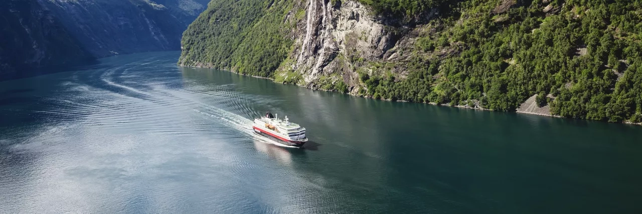 Hurtigruten's MS Nordly ship crossing through cliffsides in Norway.