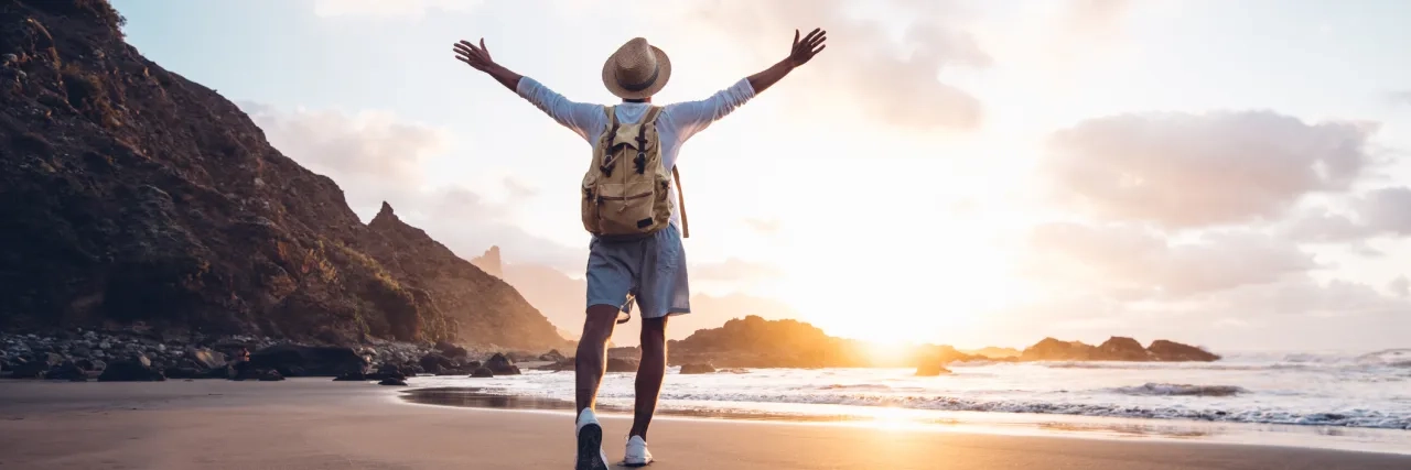 Solo traveller stretching his arms by the sea at sunrise.