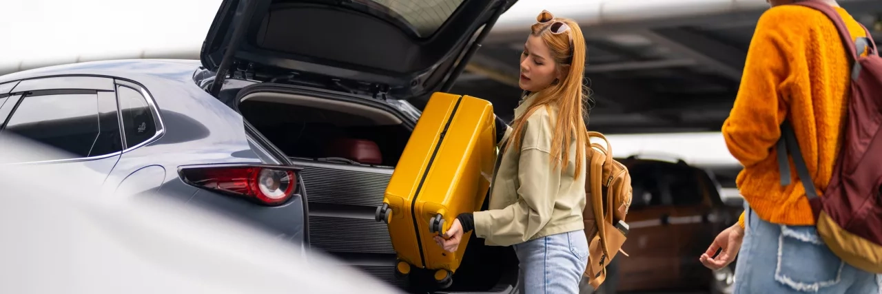Women removing luggage from car trunk in airport parking