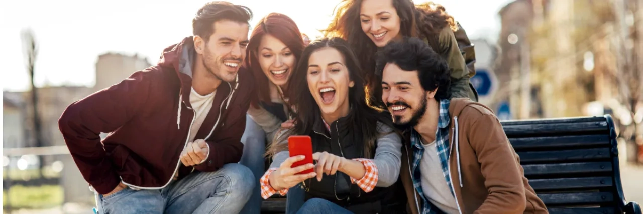 A group of friends sitting on a bench looking at a phone