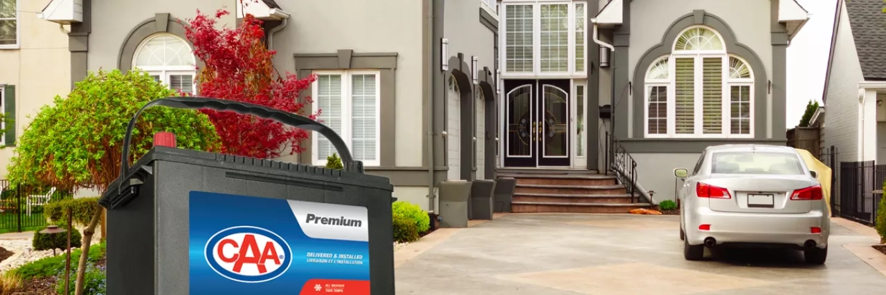 CAA Premium battery in front of a house with a car parked in the driveway.