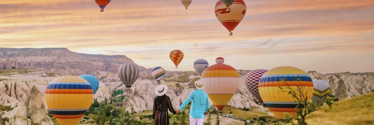 Cappadocia Turkey during sunrise, couple mid age men and woman on vacation in the hills of Goreme Capadocia Turkey, men and woman looking sunrsise with hot air balloons in Cappadocia