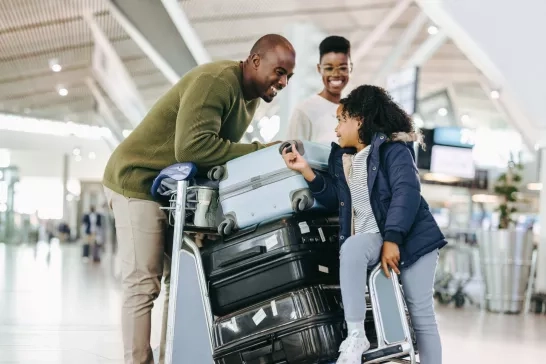 Parents and their daughter smiling together with their luggage in the airport.