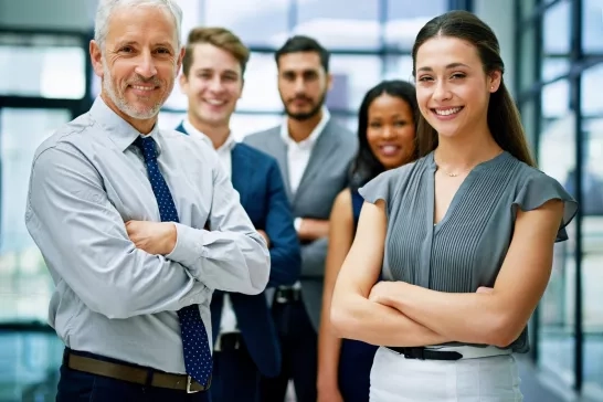 a group of 5 business people smiling at the camera in an open office setting