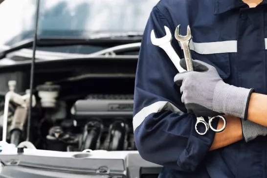 mechanic holding a wrench in front of a car