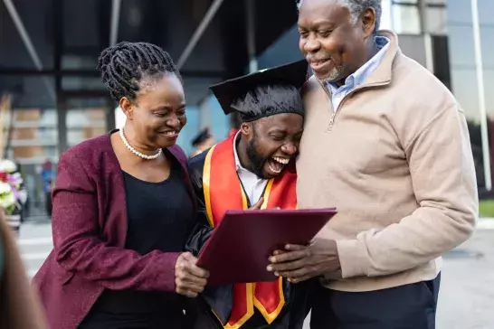 Mother and father hugging their graduating son holding a diploma in celebration