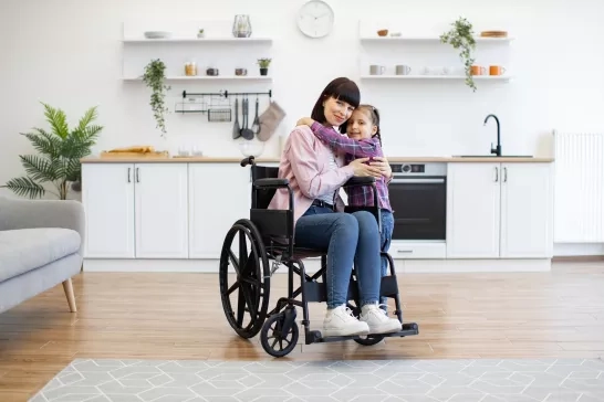 Mother sitting in a wheelchair hugging daughter at home