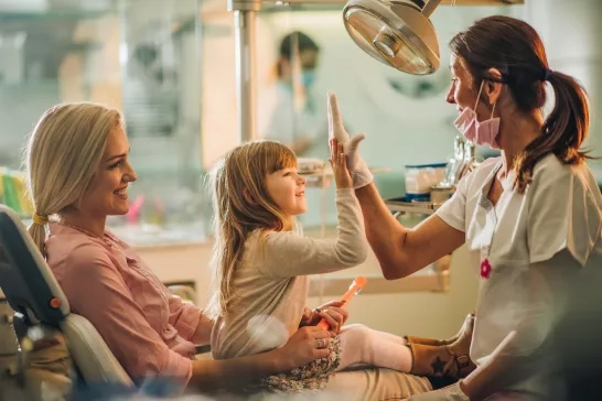 Mother and happy young girl hi-fiving dentist at dental checkup