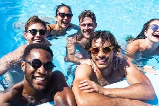 A group of young travelers relax and laugh together in a refreshing pool under the sun.