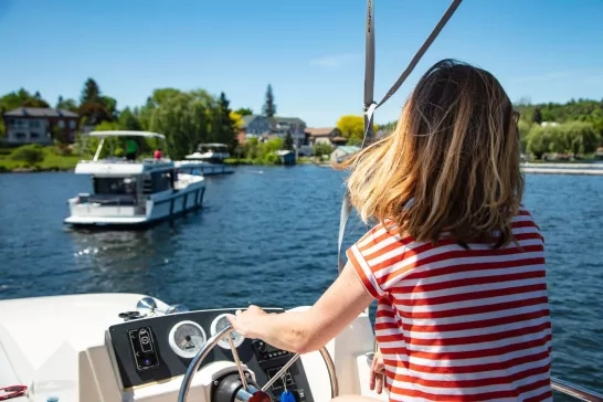 A scenic river cruise led by a woman at the helm, passing through tranquil waterways surrounded by nature.