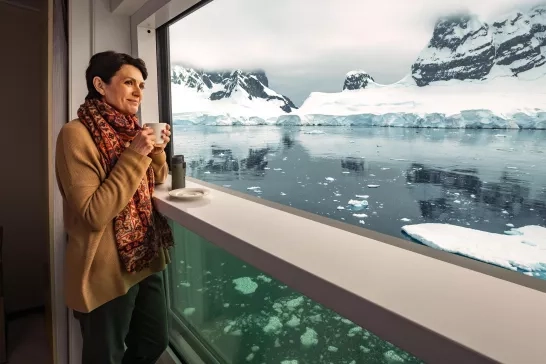 Woman stands, sipping coffee while taking in the iceberg views