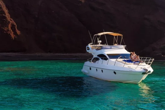 A luxurious yacht anchored in a serene, turquoise bay, where a couple enjoys the peaceful scenery and warm sun