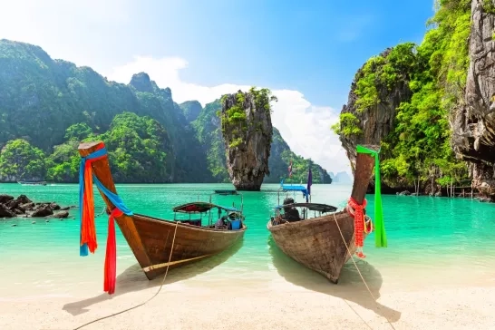 Picturesque longtail boats anchored on a pristine beach, with the towering limestone cliffs of James Bond Island in the background